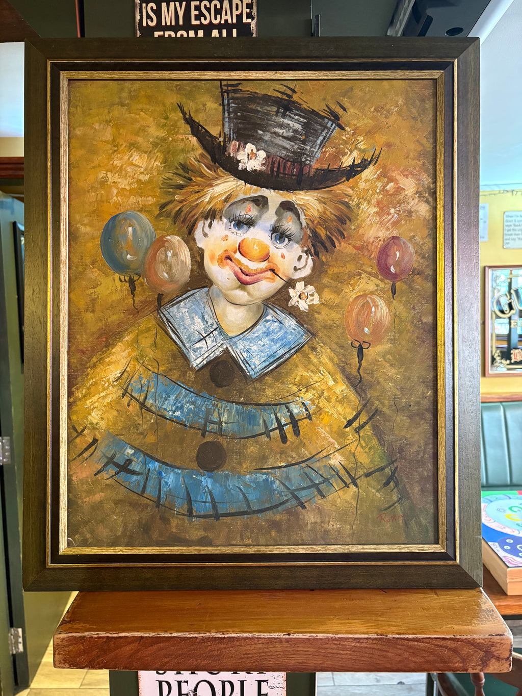 Framed clown portrait with a black top hat, blue collar and balloons against a golden background.
