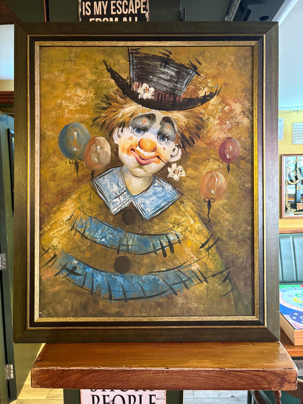 Framed clown portrait with a black top hat, blue collar and balloons against a golden background.