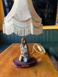 Figural table lamp with a kneeling woman holding grapes beneath a cream fringed shade
