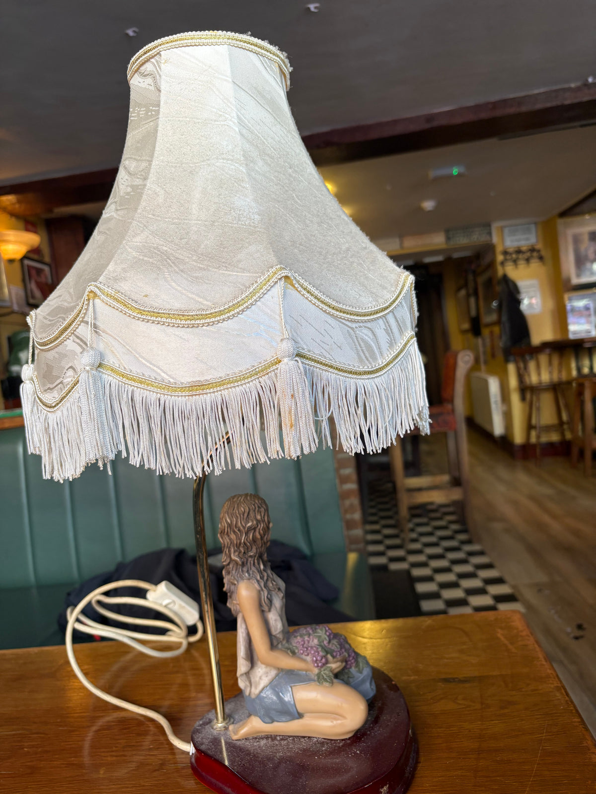 Side view of kneeling-woman table lamp with cream scalloped shade, fringe and tassels