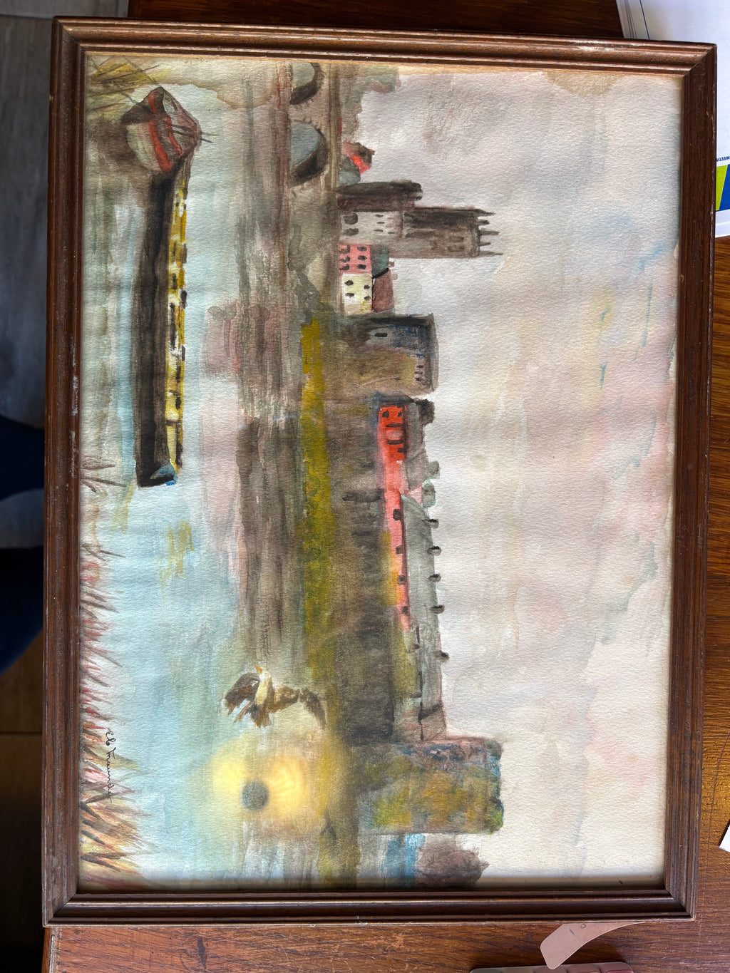 Framed riverside town picture photographed sideways, with stone towers, colourful houses and boats.