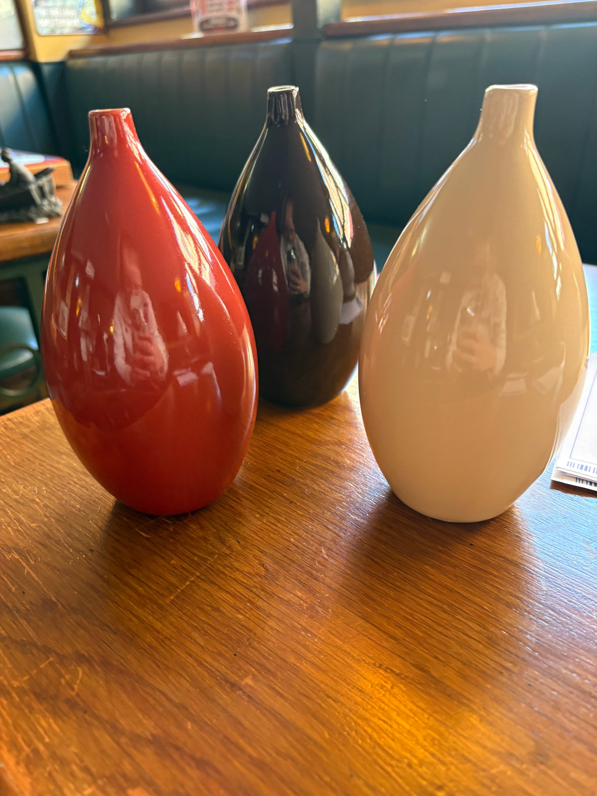 Three glossy teardrop-shaped ceramic bud vases in red, dark brown and cream