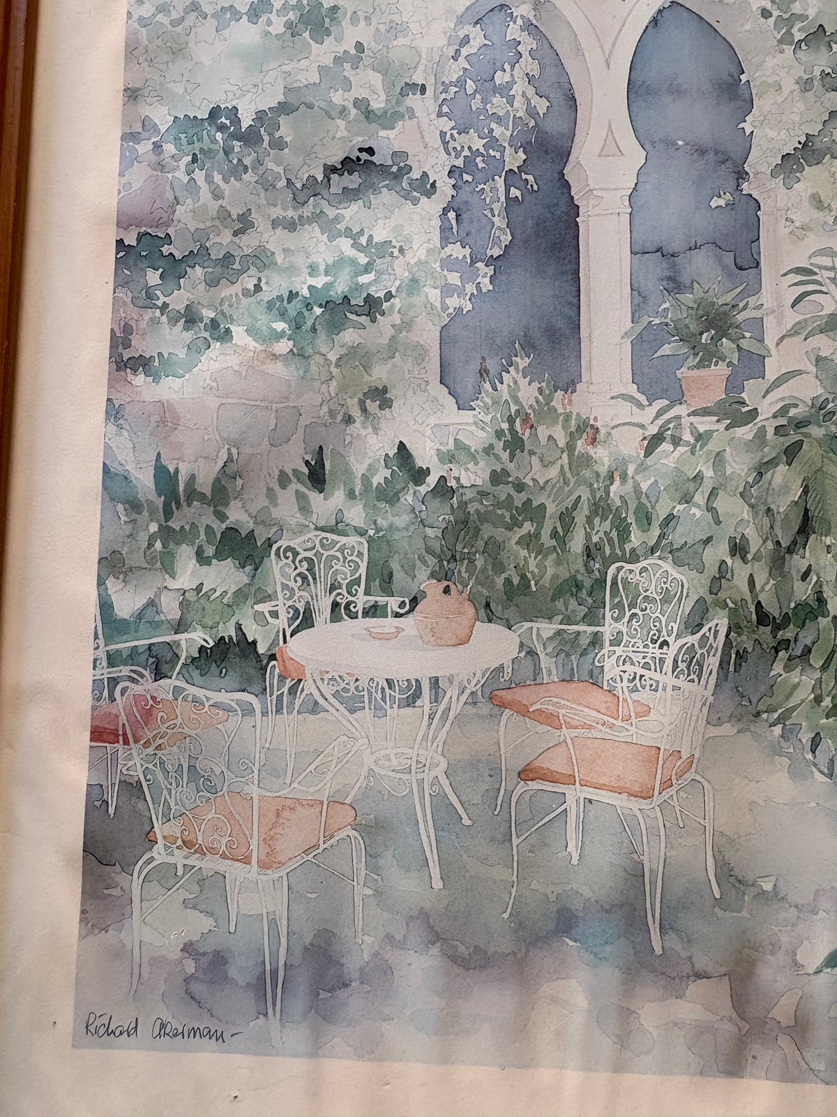 Courtyard picture detail showing white garden chairs with peach cushions around a table beneath pointed arches.
