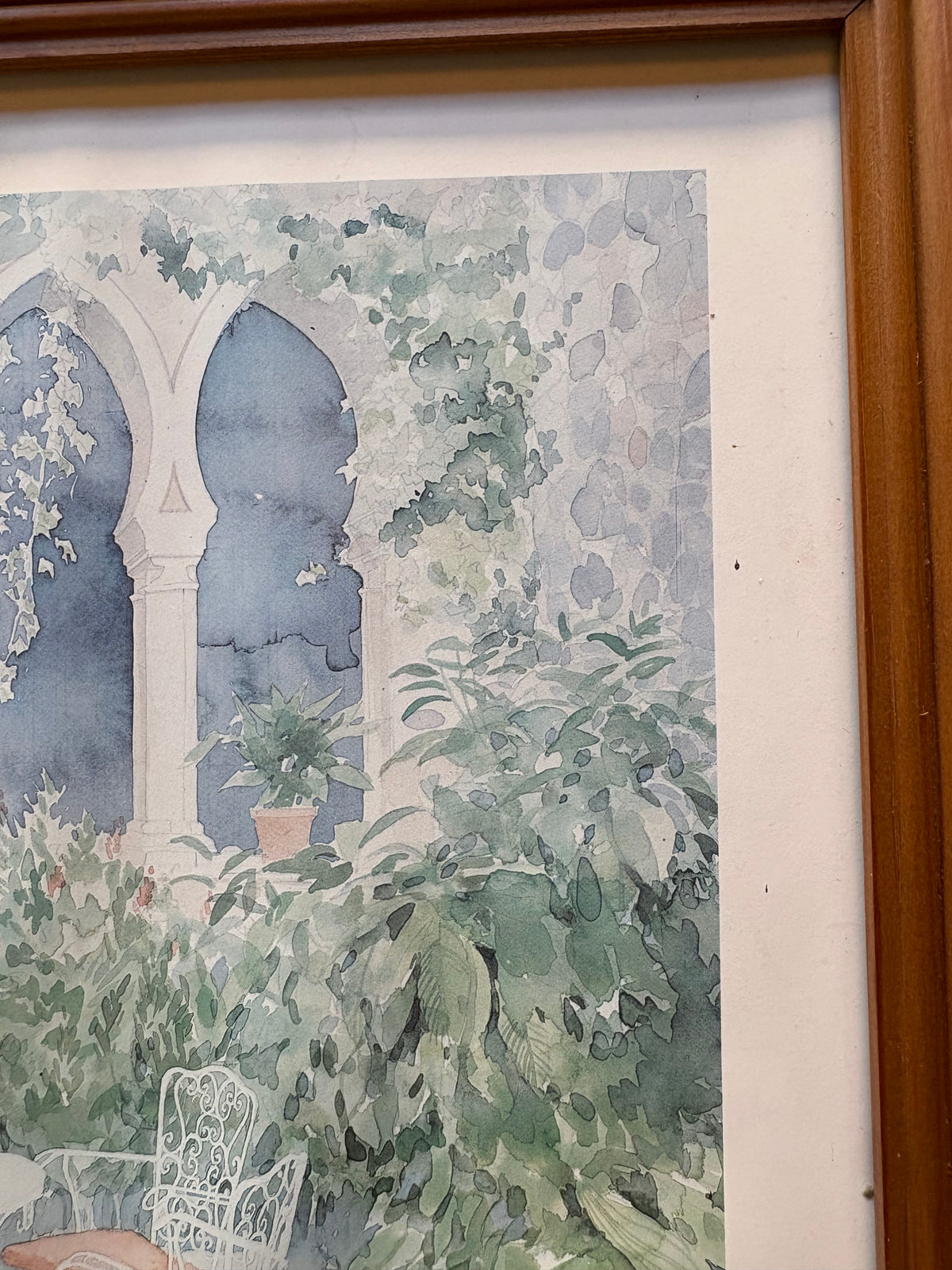 Upper-right courtyard detail showing pointed stone arches, a potted plant and dense green foliage.