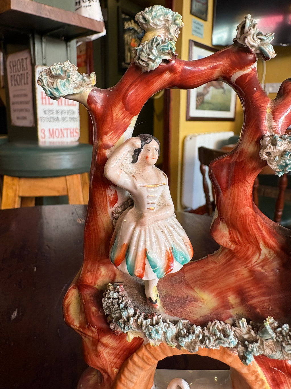 Angled detail of the female figure beside the red tree trunk, with raised foliage along the ledge