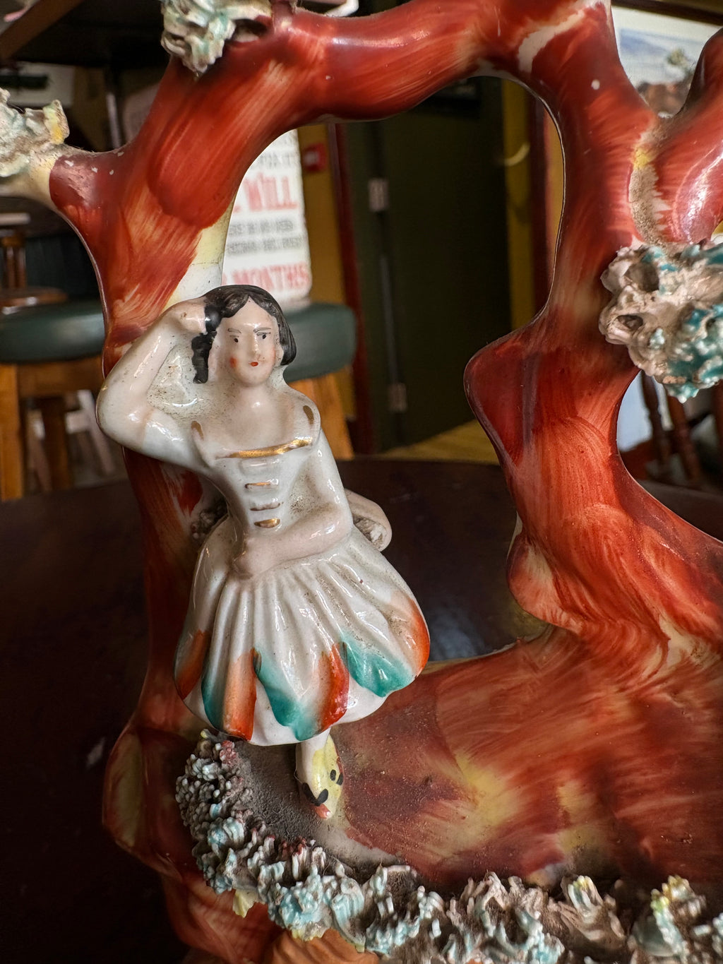 Close-up of the female figure in a white dress with green and orange skirt panels beneath a red tree arch