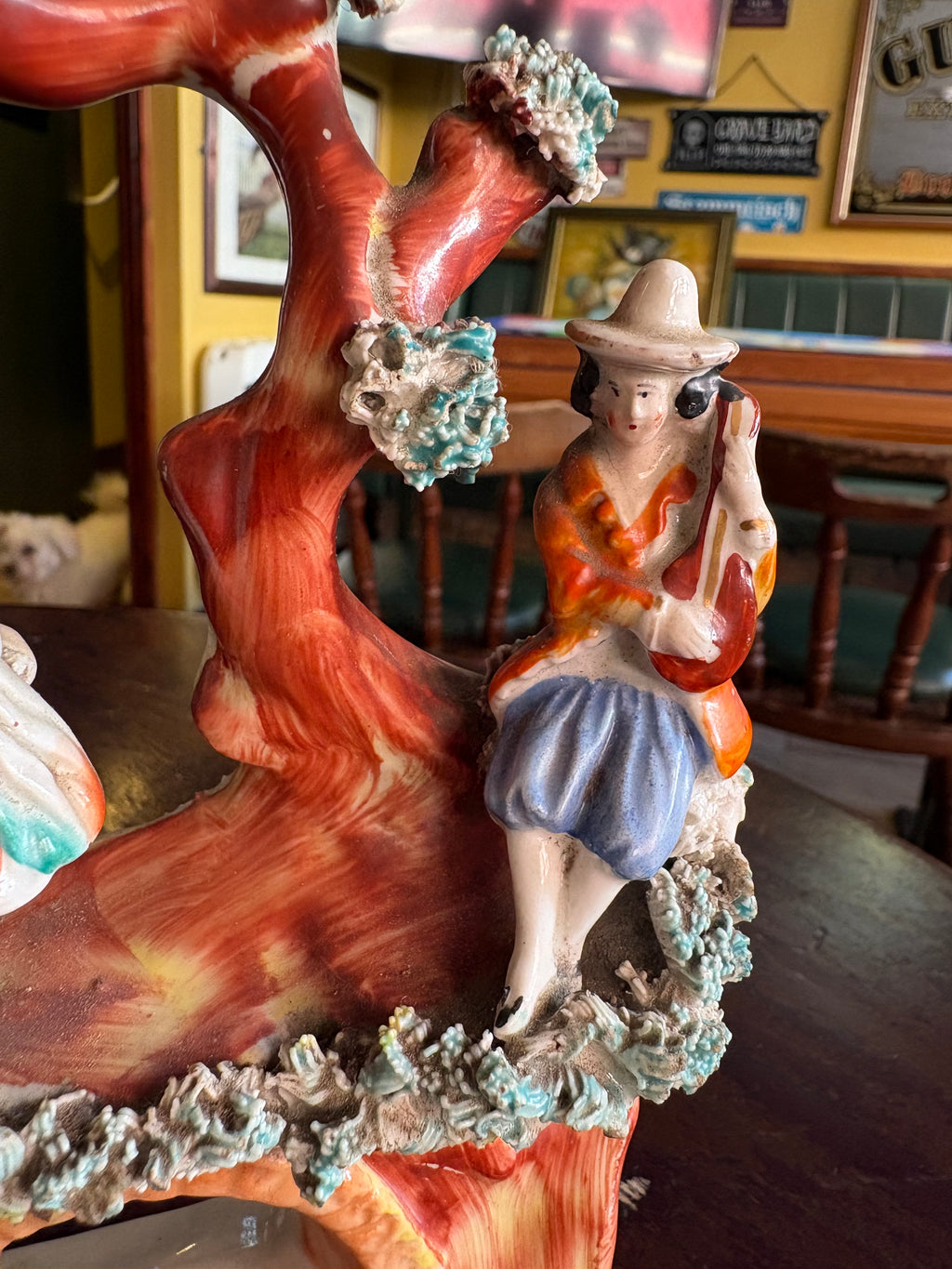 Detail of the instrument-playing figure, broad-brimmed hat and textured foliage on the figurine group