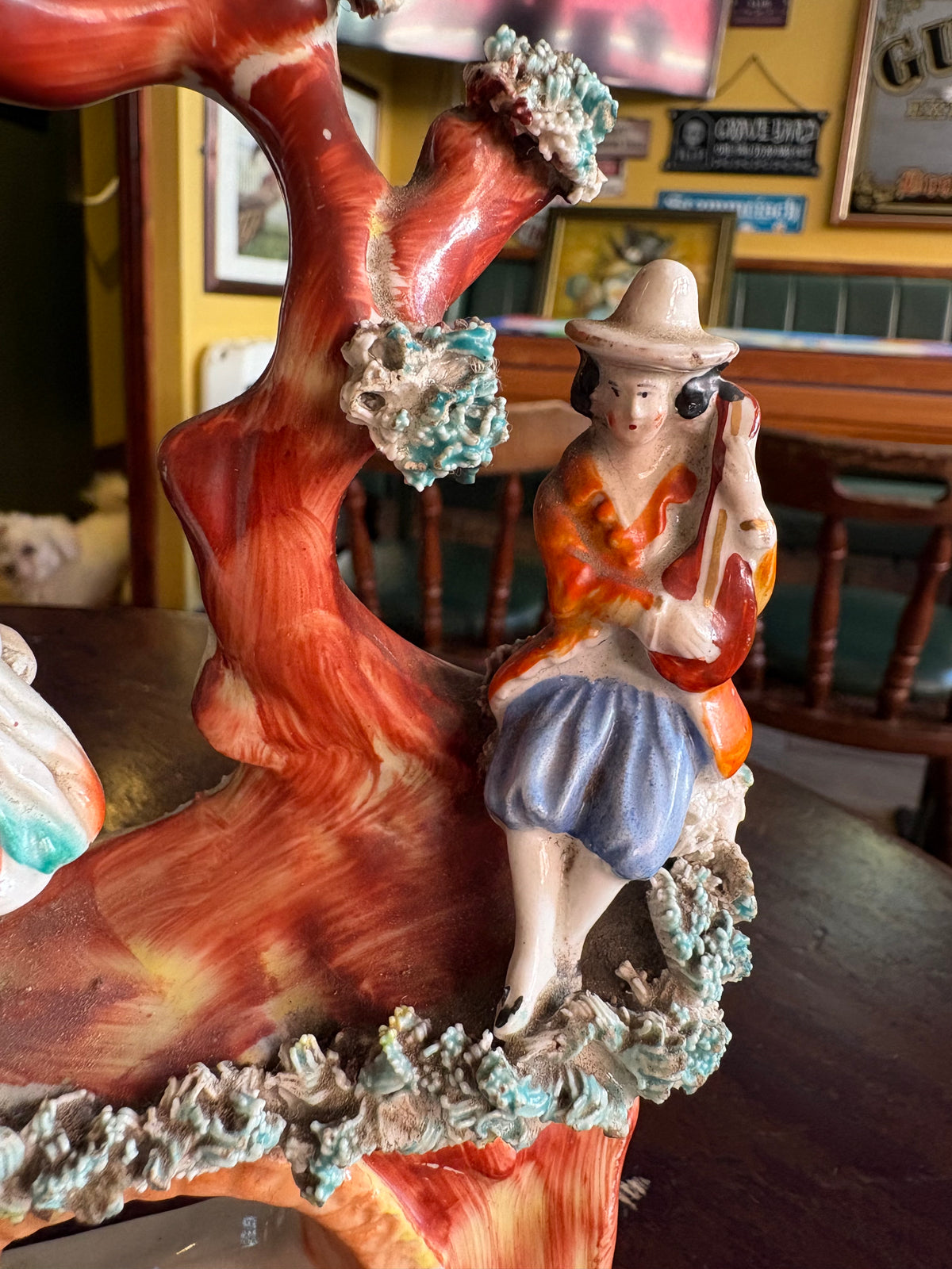 Detail of the instrument-playing figure, broad-brimmed hat and textured foliage on the figurine group