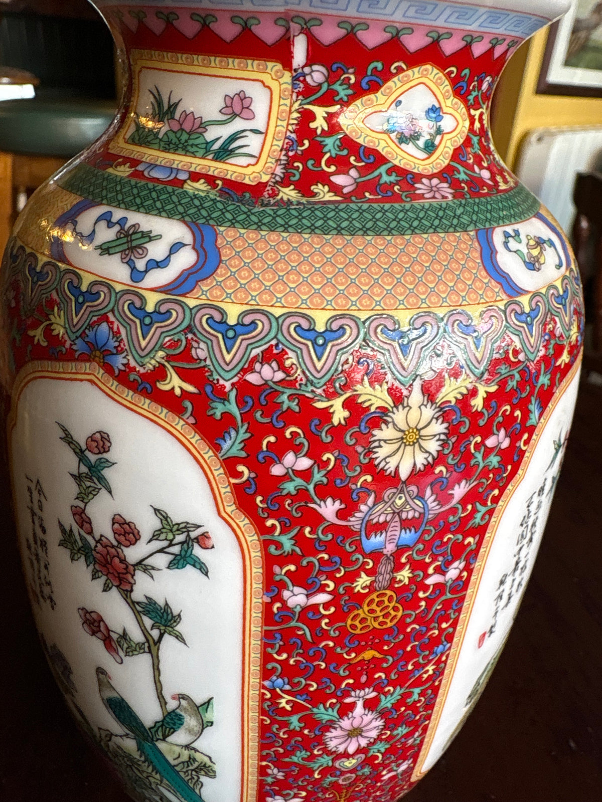 Close-up of red porcelain vase showing floral scrollwork and multicoloured decorative bands