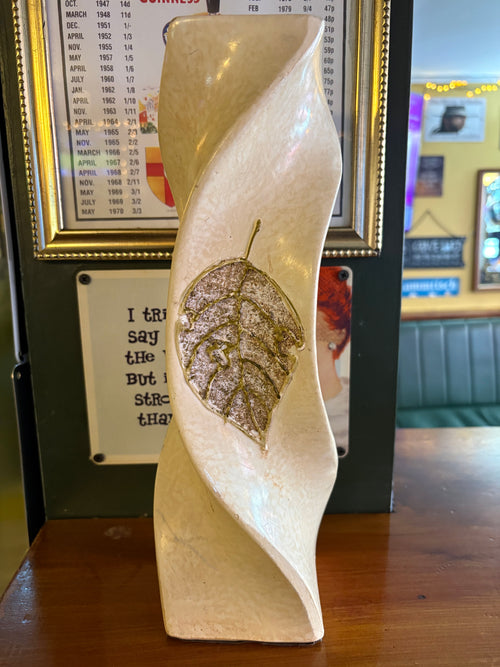 Tall cream twisted sculptural vase with a gold-coloured leaf motif on the front