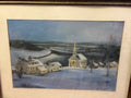 Framed winter village scene with a steepled church, snow-covered houses and fields beneath a blue sky.