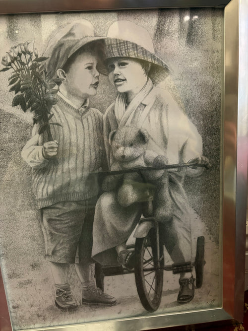 Framed monochrome picture of two children with flowers and a teddy bear beside a tricycle.