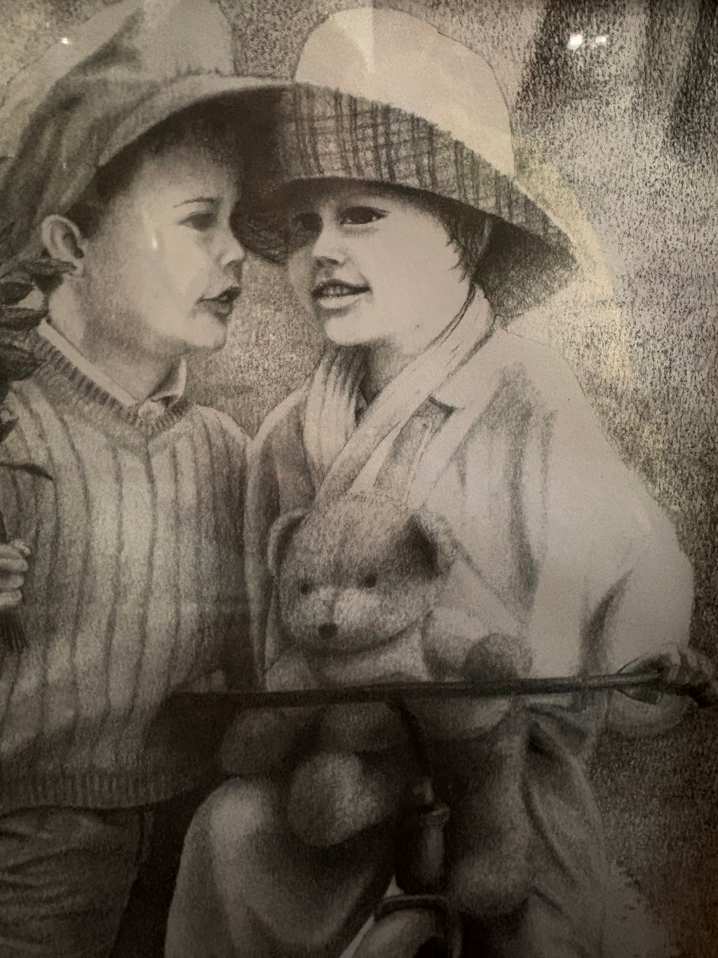 Close-up of the two children wearing hats, with a teddy bear above the tricycle handlebars.