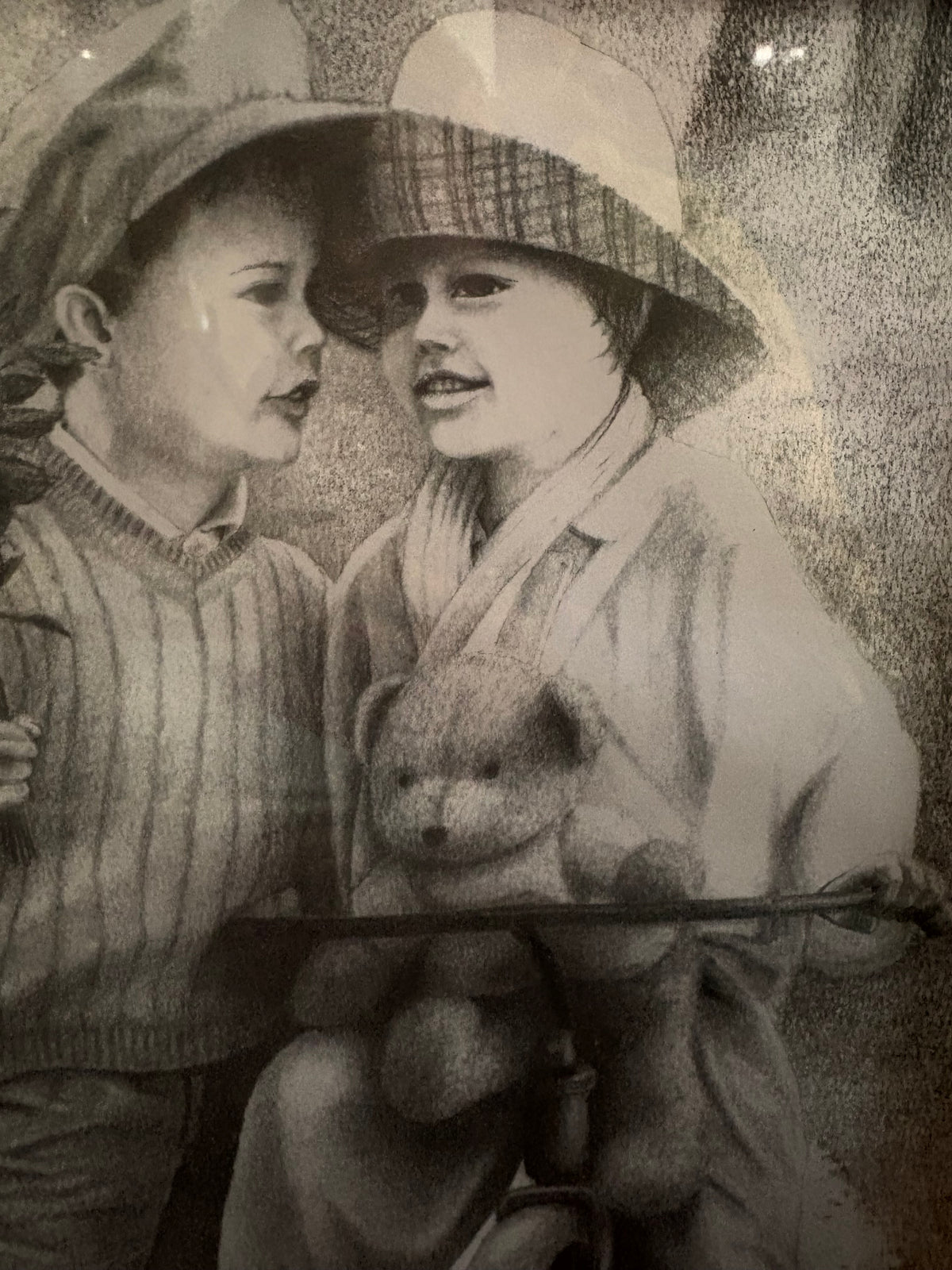 Close-up of the two children wearing hats, with a teddy bear above the tricycle handlebars.