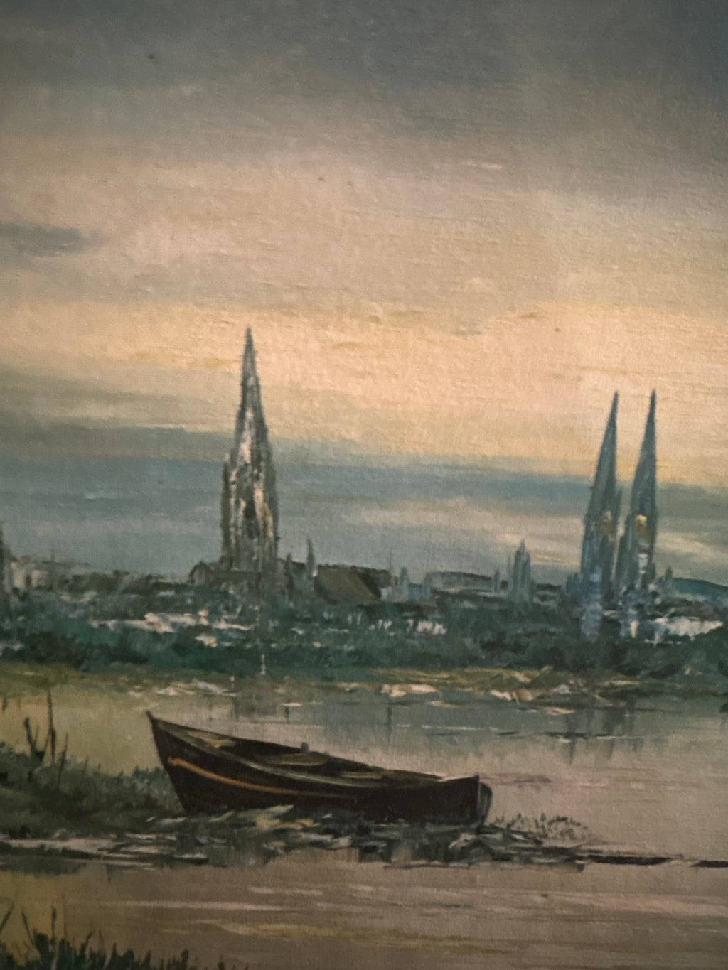 Close-up of a rowboat on the riverbank with distant church spires beneath a glowing sky.