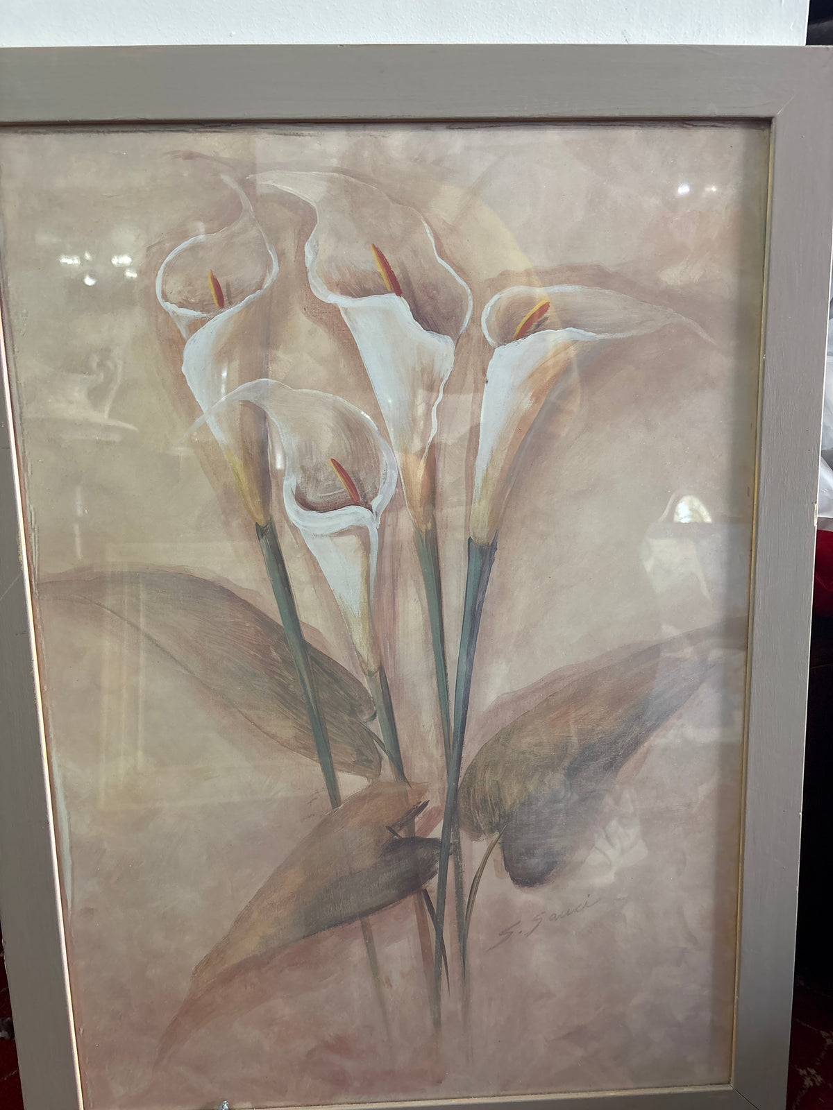 Framed floral picture of white calla lilies with long green stems and muted brown leaves.