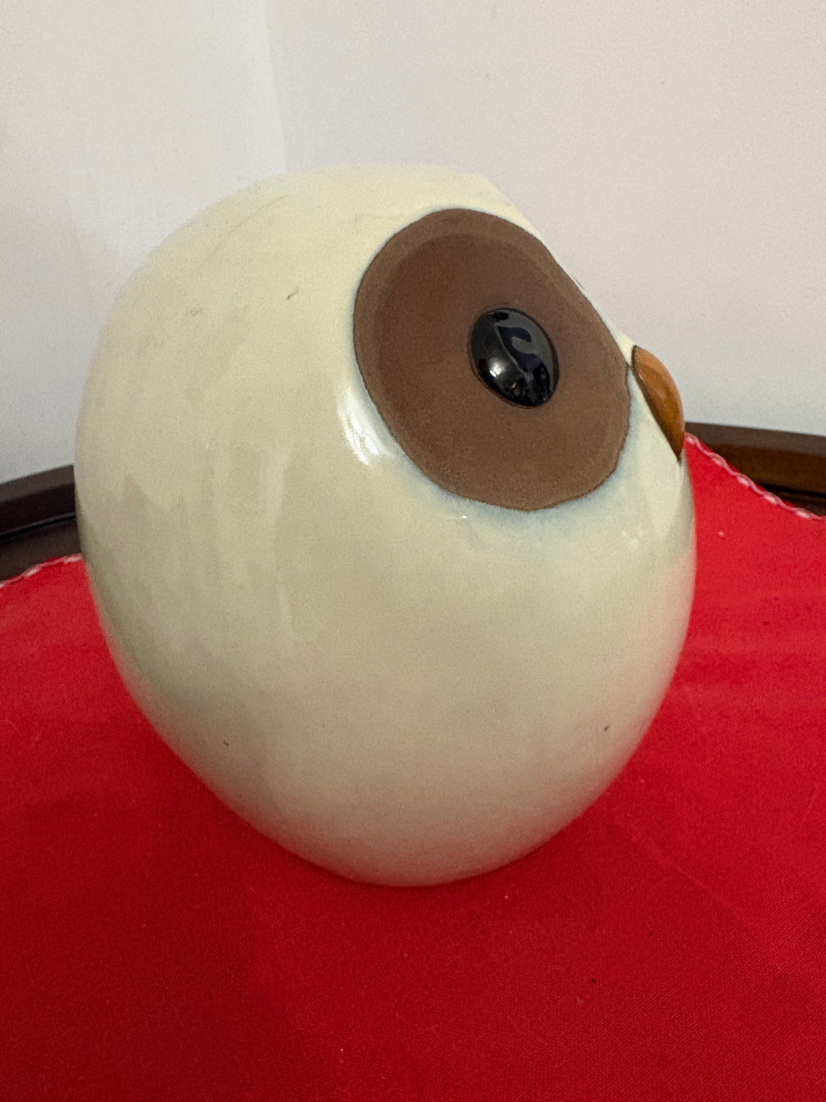 Side view of the rounded cream owl figurine showing one brown eye patch and projecting amber-coloured beak