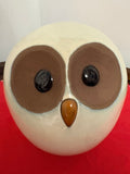Close front view of a rounded cream owl figurine with large brown eye patches, black eyes and amber-coloured beak