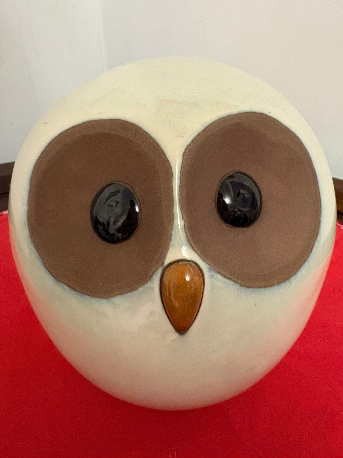 Close front view of a rounded cream owl figurine with large brown eye patches, black eyes and amber-coloured beak