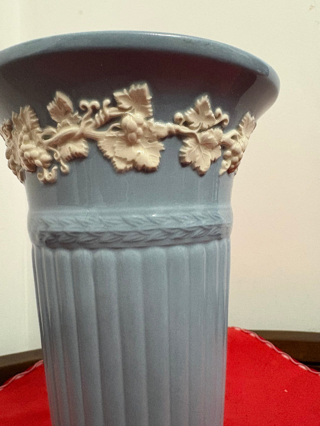 Close-up of cream grape leaves and grapes around the blue-grey trumpet vase rim