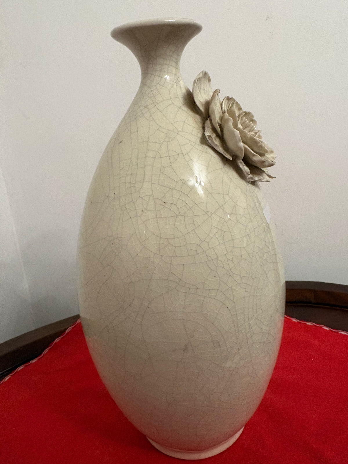 Angled view of rounded off-white vase with crackled surface and applied flower near the neck