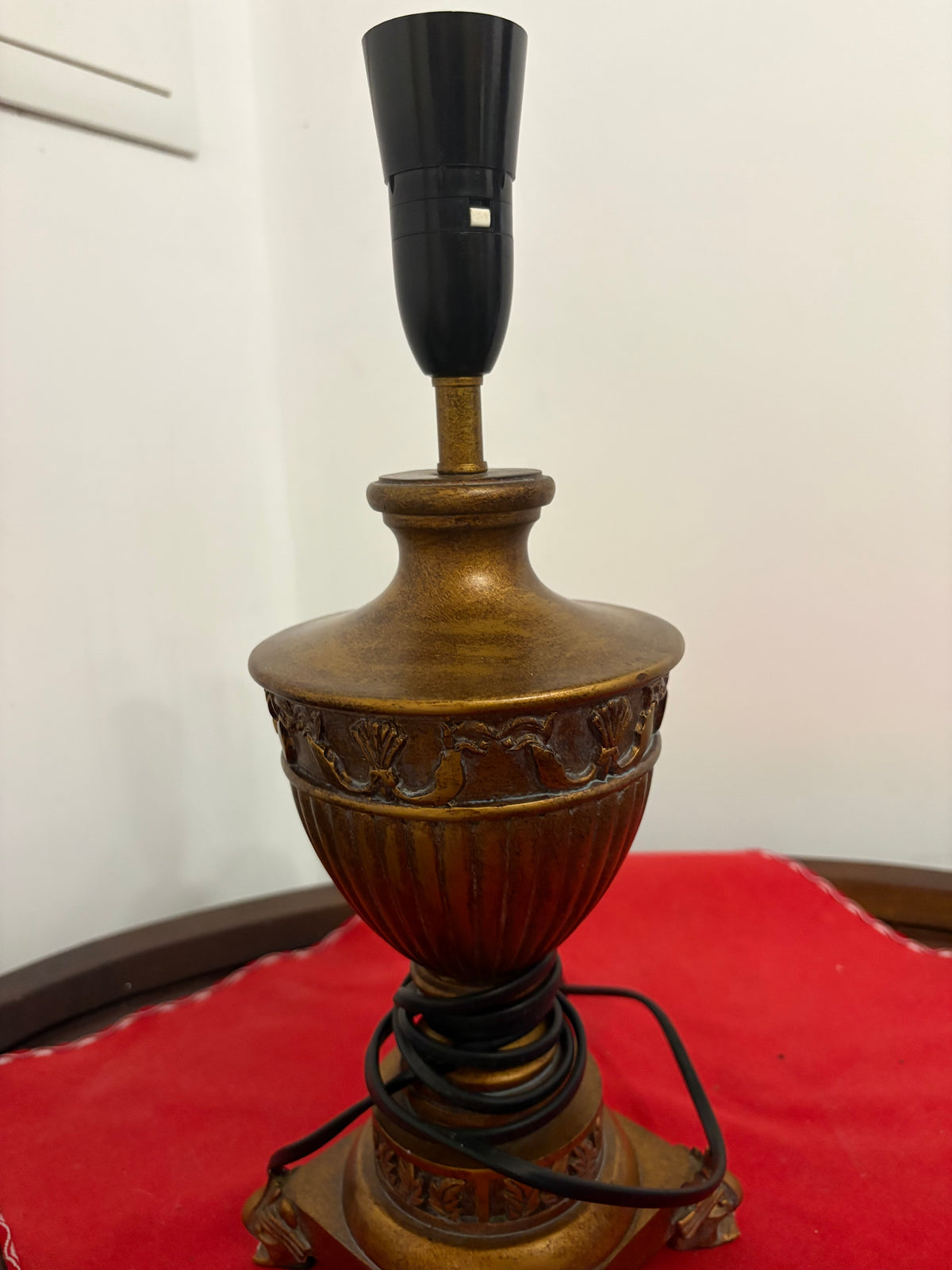 Angled view of brass urn table lamp showing garland decoration and cord wrapped around its base