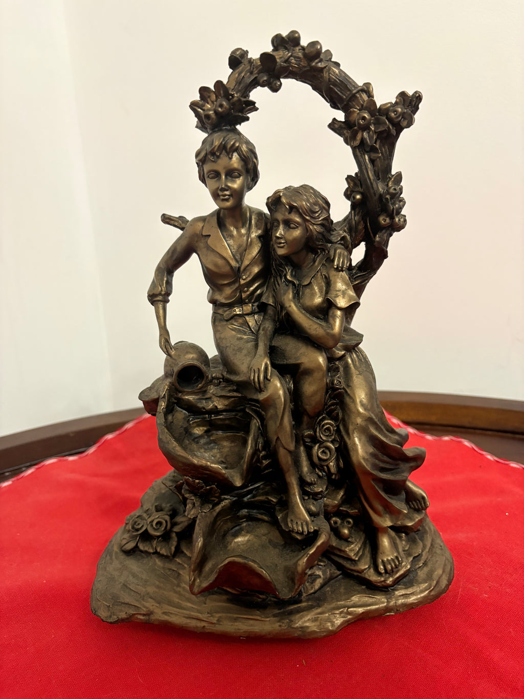Bronze-coloured figurine of a seated young couple beneath a flower-covered arch, with cascading bowls at the base