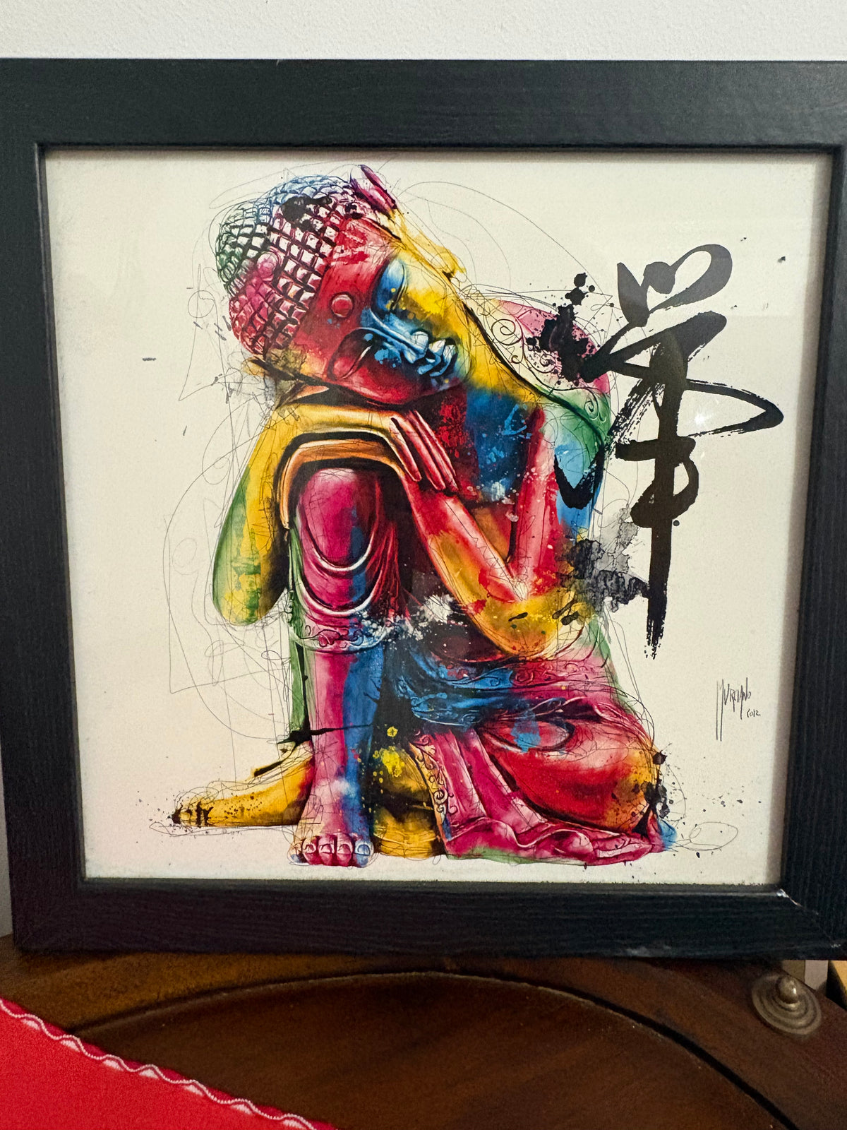 Colourful seated Buddha print with black calligraphic marks in a black frame.