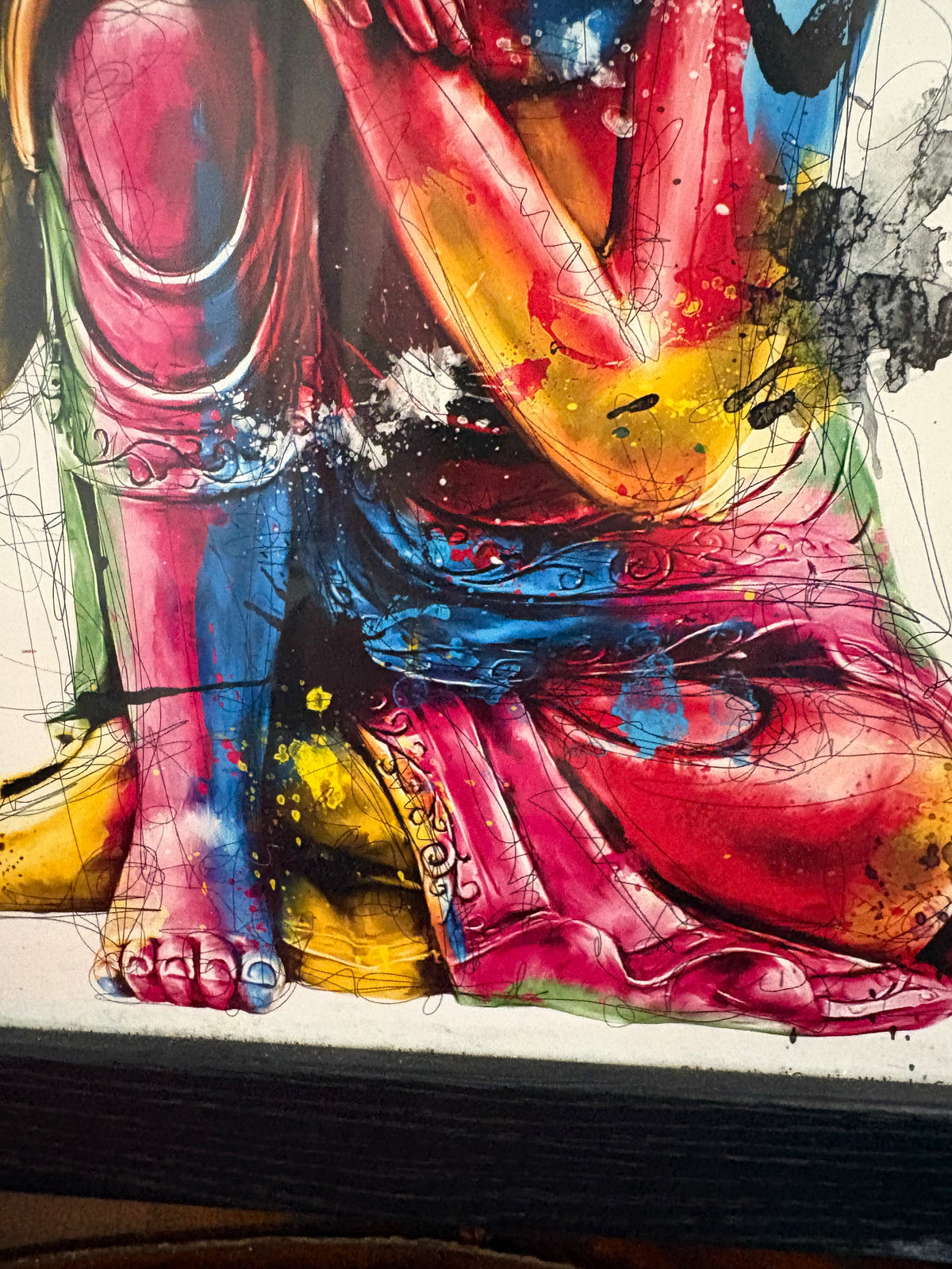 Lower detail of the Buddha print showing colourful robes, feet and black frame edge.